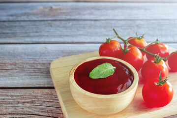 Tomato ketchup sauce and basil in a wooden cup and tomato fruit placed on a wooden tray on wooden table. close up shot.