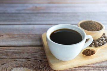 Black hot coffee in a white ceramic mug and roasted coffee powder And a wooden spoon placed on a wooden tray.