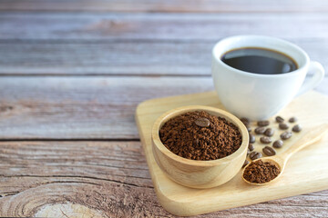 Ground coffee powder in a wooden cup and in a wooden spoon with a white coffee cup and coffee beans all on a wooden tray.