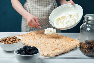 Woman spreads whipped sweet cream on meringue cake on a white vintage wooden table.