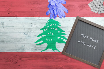 Lebanon flag background on wooden table. Stay Home writing board, surgery gloves, pills with minimal national Covid 19 concept.