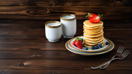 Stack of classic american pancakes with fresh blueberries, strawberries, forks and two caps of milk.