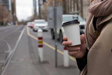 Woman Holding Coffee Waiting for Tram on City Street
