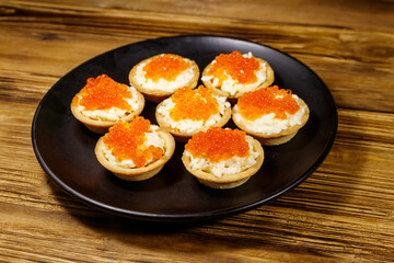 Tartlets with red caviar and soft cheese on a wooden table