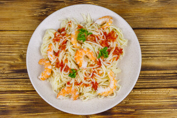 Spaghetti pasta with prawns, tomato sauce and parsley on wooden table. Top view