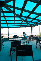 The girl is sitting in a summer cafe. Blue transparent roof in a cafe