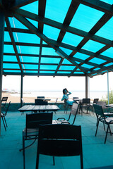The girl is sitting in a summer cafe. Blue transparent roof in a cafe