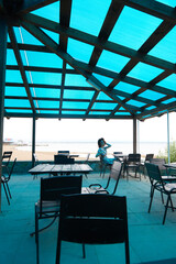The girl is sitting in a summer cafe. Blue transparent roof in a cafe