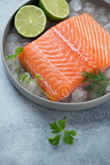Raw iced salmon fillet with fresh parsley, dill and lime, vertical shot on a light-blue stone surface, close-up