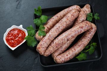 Cast-iron tray with raw fresh pork and poultry sausages, horizontal shot on a black stone background