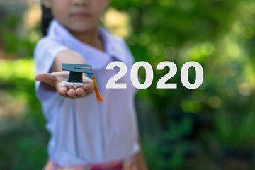 Education and online graduate certificate program concept: Schoolgirl outstretched arms with Class of 2020 with graduation cap on green nature background