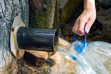 A girl pours clean water from a forest spring into a plastic bottle on a hot summer day.