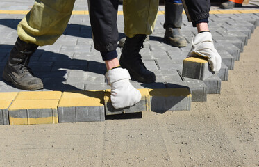 A worker puts paving slabs in straight rows, builds a pedestrian road.