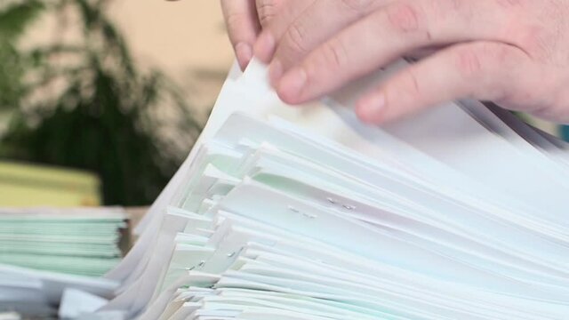 Man leafing through a large stack of documents in the office. Hands close up.