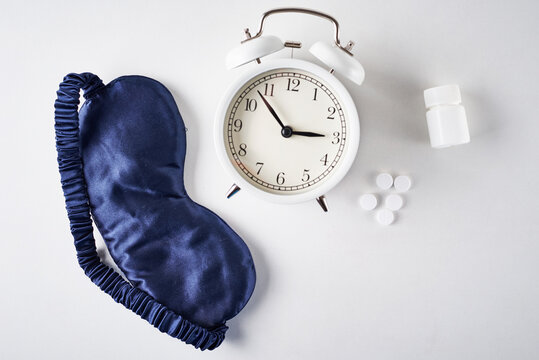 Insomnia, Depression And Sleeping Trouble Concept. Alarm Clock, Sleeping Mask And Pills On A White Background, Top View