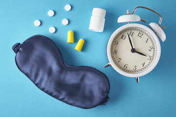 Insomnia problem concept. Alarm clock, sleeping mask, ear plugs and pills on a blue background, top...