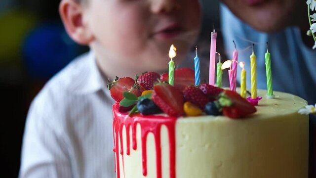 hand lighting candles in birthday cake. Adorable happy blond little kid boy celebrating his birthday. Child blowing candles on homemade baked cake, indoor. Colored party for school children