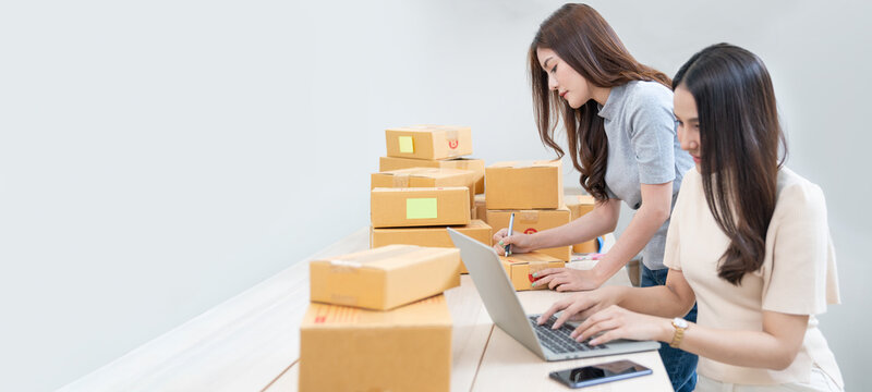 Startup small business owner working with computer at workplace. Freelance two woman seller check product order. Packing goods for delivery to customer. Online selling. E-commerce. Online Shopping
