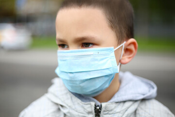 A boy with a medical mask on his face stands in the middle of a busy street.