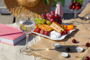 A glass of clean sparkling mineral water stands against a plate of fruit at a family picnic. The benefits of mineral sparkling water.