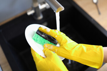 Gloved hands wash dishes under pressure water