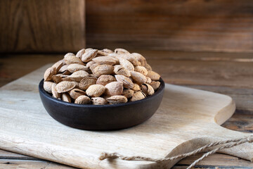 Salty Almonds in shells in round bowl on rustic wooden background 