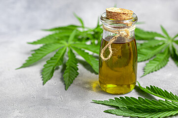Cannabis oil in a transparent bottle and hemp leaves on a gray background.