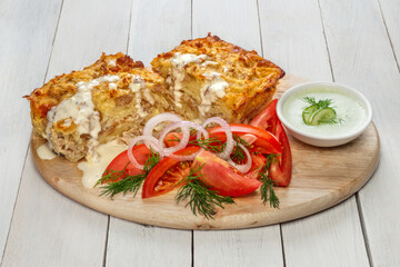 Potato casserole with minced meat and cucumber-dill sauce on a light wooden board