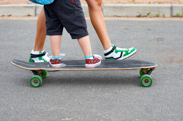 Mom and kid ride a longboard. Time with the kids. Time for family. Feet on a skateboard close-up. family activities. Summer outdoor activities. mom teaches a child to ride. Copy space. 