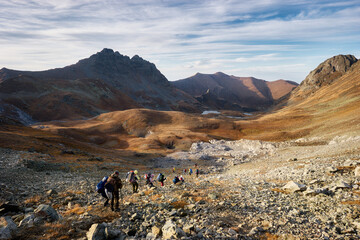bright panorama of the Caucasus mountains in the sunny autumn, a group of tourists rises uphill. Arkhyz, Russia
