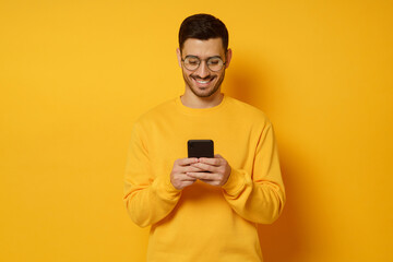 Young trendy man in glasses and sweater, feeling happy about conversation in text messages with...