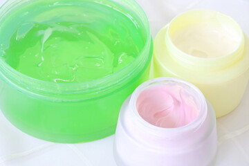 Close up group of yellow, pink and green (aloevera gel) cream in container on white fabric background, side view.