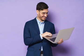 Business man holding open laptop in hands, browsing web pages or chatting with friends and colleagues online, feeling happy, isolated on purple background