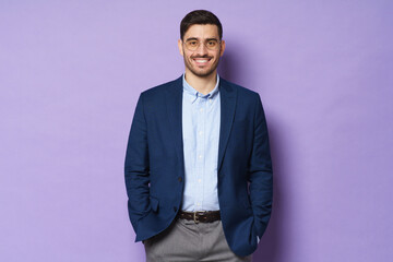 Business guy dressed in jacket and shirt, wearing glasses, standing in confident relaxed pose, hands in pockets, smiling happily, isolated on purple background