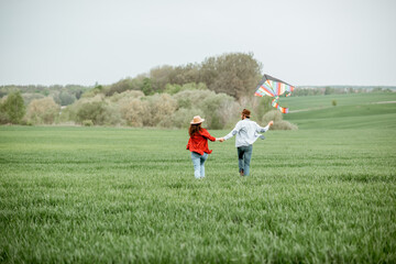 Happy couple having fun together, playing with kite on the greenfield. Happy couple expecting a baby and young family concept
