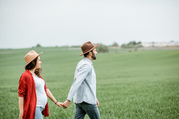 Pregnant woman with her man having fun together, walking on the greenfield. Happy couple expecting a baby, young family concept