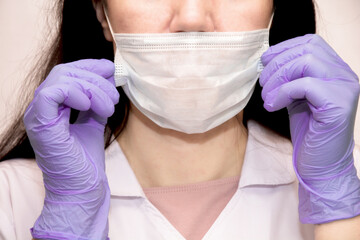 A young woman in lilac medical gloves puts a protective mask on her face . A confident girl, a female doctor in a medical mask.Protection AGAINST covid-19 coronavirus