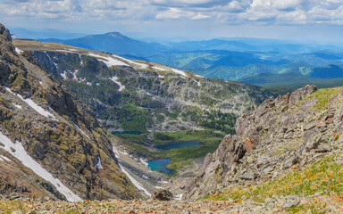Over the mountain gorge. Rocky slopes, snowfields and small lakes. Spring in the mountains.