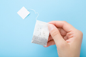 Young woman hand holding bag of black tea on light blue table background. Pastel color. Closeup. Point of view shot. Top down view.