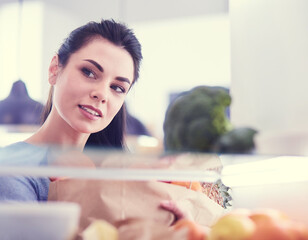 Smiling woman taking a fresh fruit out of the fridge, healthy food concept