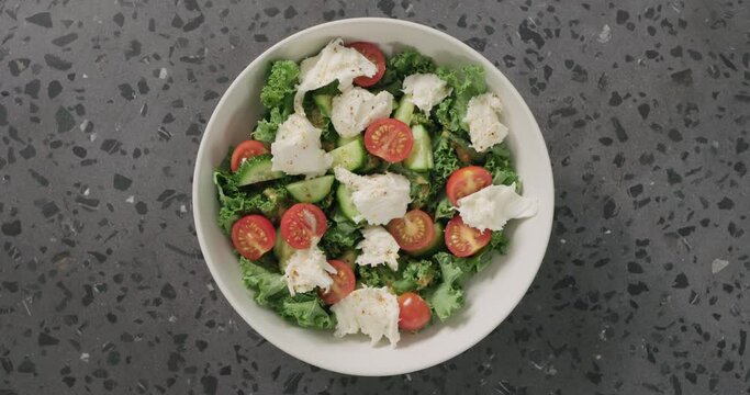 Top view man hands eat salad with kale, tomatoes cucumbers, and mozzarella in white ceramic bowl on concrete background