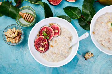 Healthy breakfast. A bowls  of porridge with pears slices and walnuts and porridge with figs on blue background. Two bowls. Flat lay. Copy space. Top view.