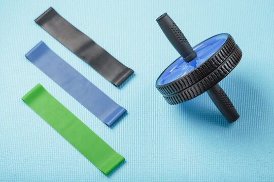 Set for sports, blue roll for abs muscles, elastic bands for fitness on a blue training Mat.