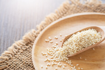 White sesame seeds in a wooden spoon on wood table.