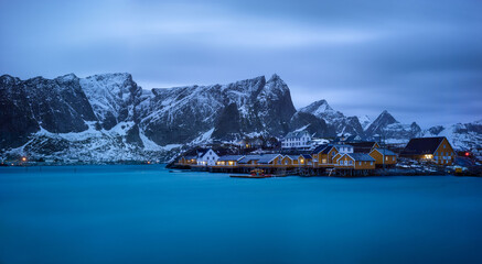 A panoramic evening shot of classic yellow rorbu under cloudy sky and snowy mountain in Reine, Lofoten island, Norway