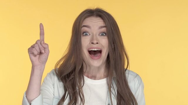 Close-up portrait of young woman showing idea gesture. Yellow background.