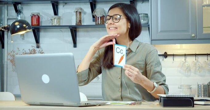 Young woman teacher showing pictures with the alphabet, learning letters and words, studying with a child or kids online using a laptop at home. Preschool Online Education Concept.