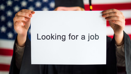 A graduate in a mantle and cap is holding a poster about job search. Employment in the USA