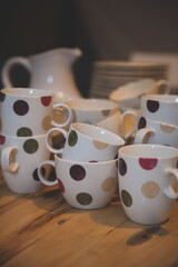 Close-up of tableware on the table. Many cups of polka dots stand on a wooden table in a darkened room. A party. A lot of people are expected. Toning