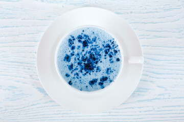 Cup of blue matcha latte on a white-blue wooden background. Top view.